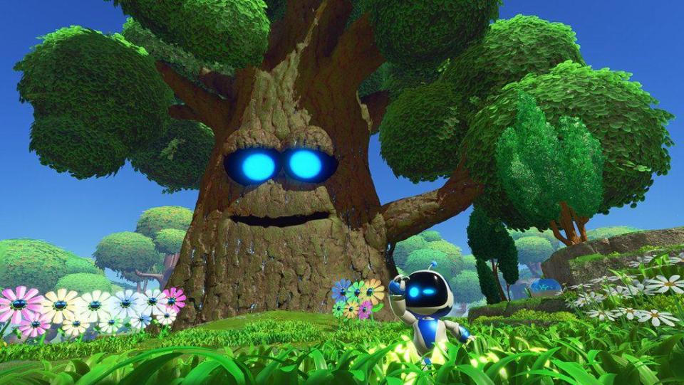 A small robot with a white body, black screen for a face and two bright blue eyes frolics in a green field full of colorful, identical flowers arranged in neat rows. Behind him, a giant tree with a smiling face and bright blue eyes looks over the jolly scene.