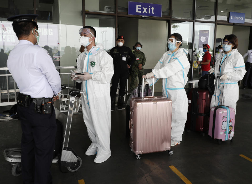Foreigners wear protective suits as they enter the departure area of Manila's International Airport, Philippines on Friday, May 22, 2020. Some airlines began flights in and out of the country as the capital eases it's lockdown while it continues to fight the spread of the new coronavirus. (AP Photo/Aaron Favila)