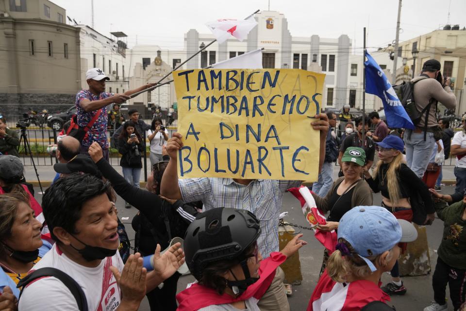 Opponents of Peruvian President Pedro Castillo celebrate his ouster outside the police station, where he arrived and his status was not immediately clear, in Lima, Peru, Wednesday, Dec. 7, 2022. Peru's Congress removed Castillo from office Wednesday, voting to replace him with Vice President Dina Boluarte, shortly after Castillo decreed the dissolution of the legislature ahead of a scheduled vote to oust him. The poster reads in Spanish: "We will also take out Dina Boluarte". (AP Photo/Martin Mejia)