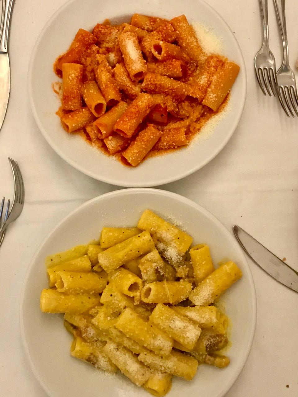 A plate of red pasta and a plate of yellow pasta shot from above on a white tablecloth