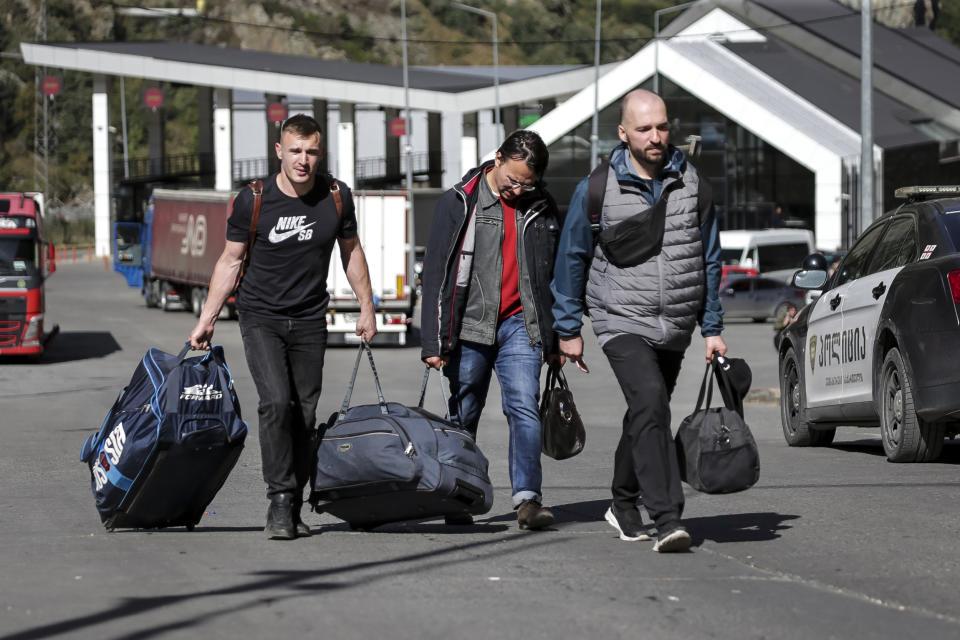 Image: Russian men carry their luggage after crossing the border at Verkhny Lars between Georgia and Russia (Zurab Tsertsvadze / AP)