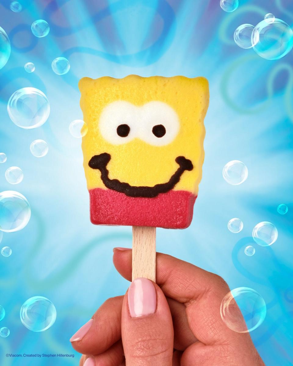 A hand holding the stick for a red and yellow smiling SpongeBob Squarepants frozen treat from Popsicle