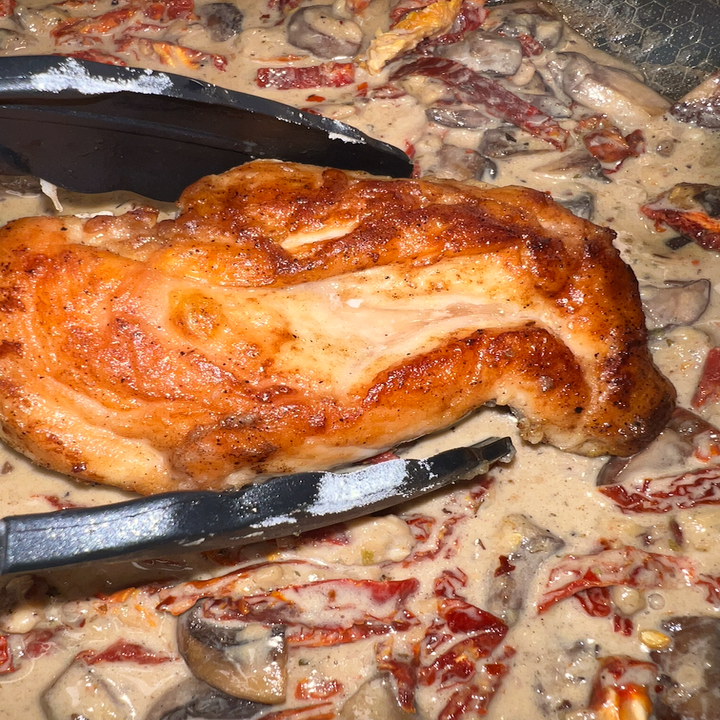 Krista using a pair of tongs to add the chicken back into the skillet