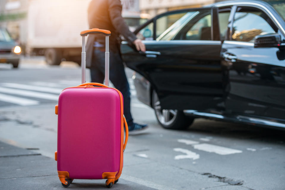 People taking taxi from an airport and loading carry-on luggage bag to the car. Luggage on the city street. Travel concept.