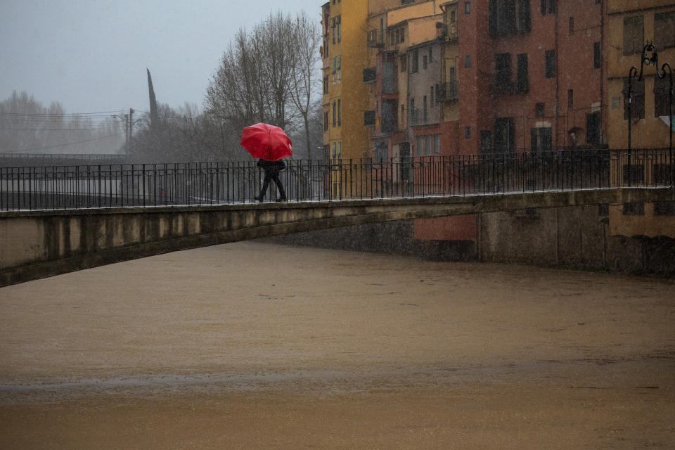 A woman holds an umbrella crossing a bridge over the river Onyar during a storm in Girona, Spain, on Thursday, Jan. 23, 2020. Since Sunday the storm has hit mostly eastern areas of Spain with hail, heavy snow and high winds, while huge waves smashed into towns on the Mediterranean coast and nearby islands of Mallorca and Menorca. (AP Photo/Emilio Morenatti)