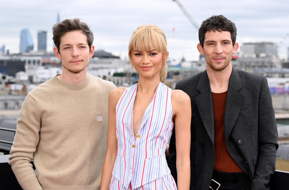 Mike Faist, Zendaya, and Josh O'Connor pose outdoors in stylish attire. Mike wears a beige sweater, Zendaya in a striped outfit, and Josh in a dark blazer