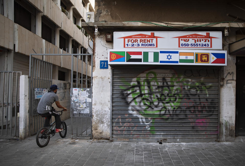 FILE - An African migrant rides his bicycle next to a a closed real-estate office with the flags of Israel, Sudan and other African countries, in Tel Aviv, Israel, Oct. 23, 2020. Sudanese asylum-seekers in Israel fear last year's normalization agreement between their new host country and Sudan could result in them being sent home. Their concerns have been magnified since the October 2021 military takeover in their homeland. (AP Photo/Oded Balilty, File)