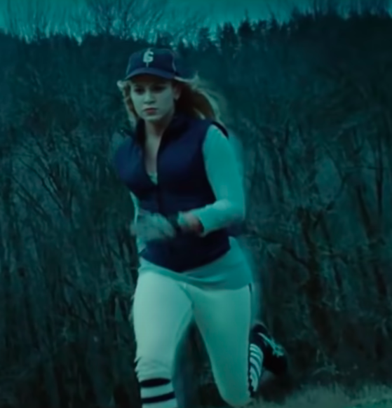 Rosalie wearing sneakers, long socks, baseball pants, a long-sleeve shirt, a winter vest, gloves, and a baseball hat