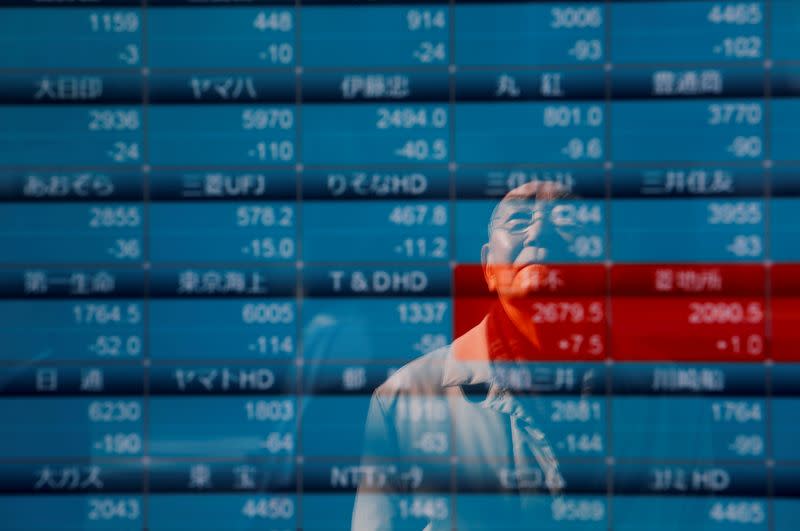 A man is reflected on a board showing stock prices outside a brokerage in Tokyo