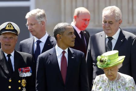 Red light reflected from the carpet illuminates Russian President Vladimir Putin as he passes U.S. President Barack Obama (C) and other leaders at a group photo for the 70th anniversary of the D-Day landings in Benouville June 6, 2014. REUTERS/Kevin Lamarque