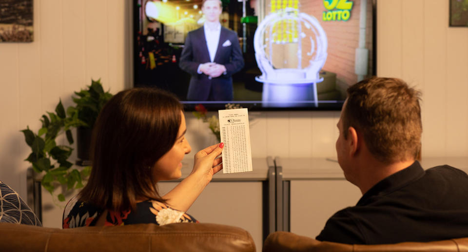 A stock image of a couple sitting on a couch watching an Oz Lotto draw.