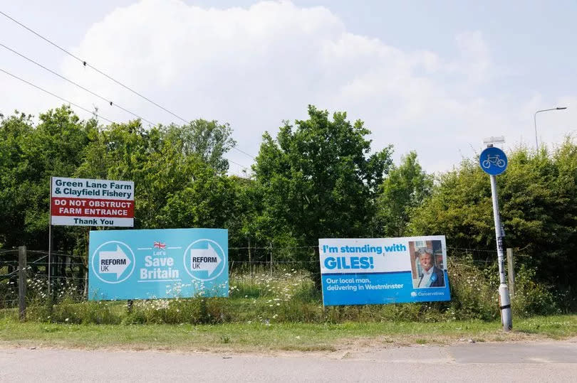 A Conservative Party campaign poster for Giles Watling, the Conservative Candidate for Clacton, and a Reform sign stand by the side of the road near Clacton-On-Sea