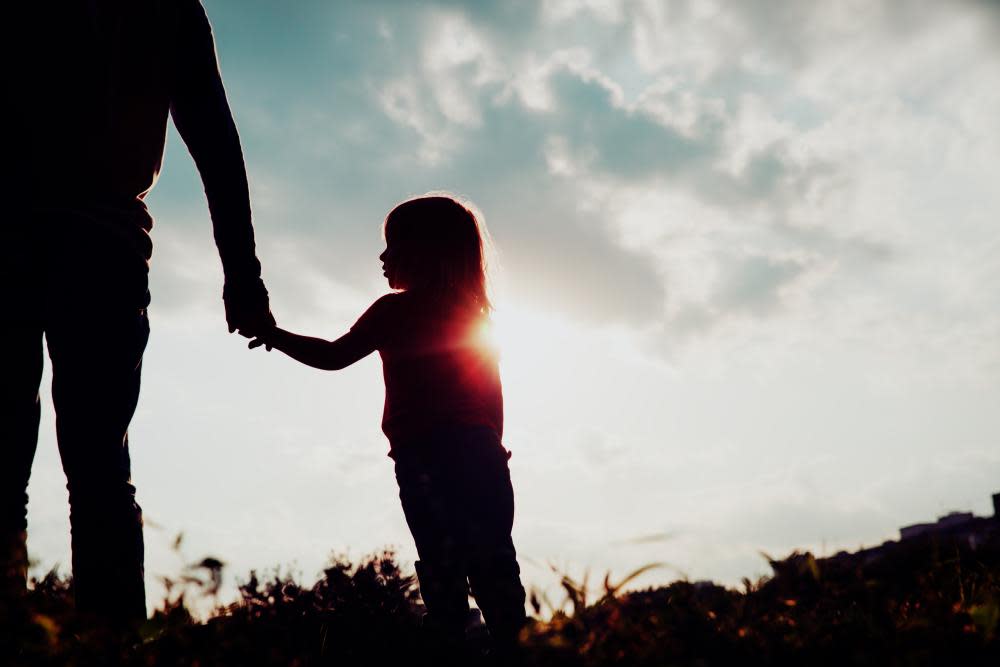 silhouette of little girl holding parent hand at sunset 