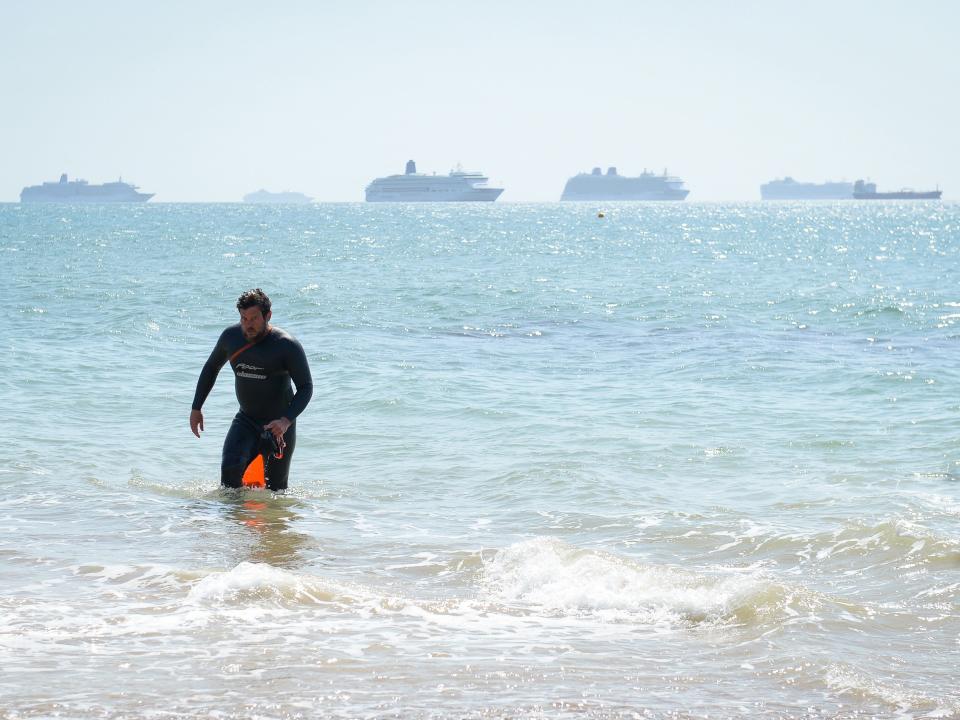 A swimmer exits the sea against the backdrop of a cruise ship off Preston beach on May 24, 2020 in Weymouth, United Kingdom