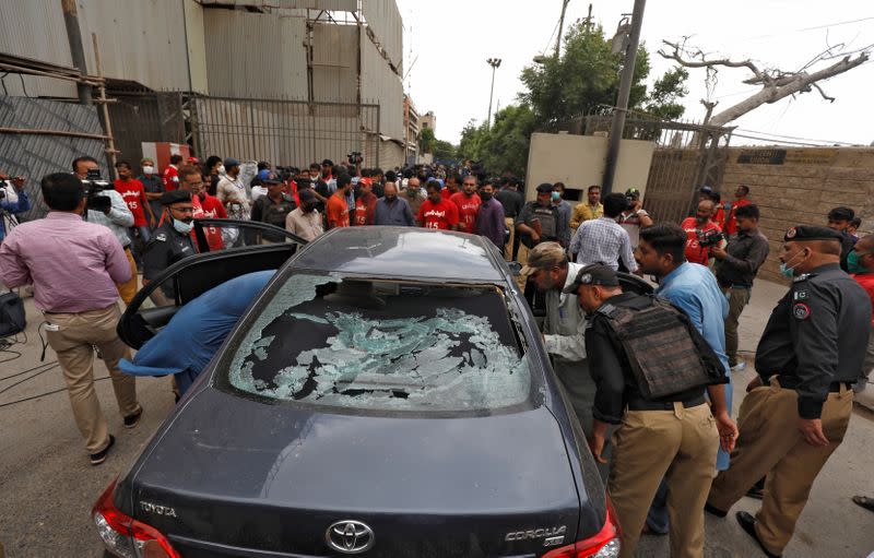 Police officers survey damaged car at site of attack at PSX entrance in Karachi
