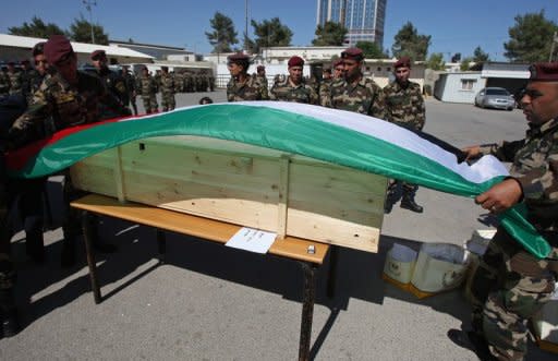 Palestinian security forces cover a coffin with the national flag ahead of the funeral procession of 91 Palestinians whose remains were returned by Israel in the West Bank city of Ramallah on Thursday
