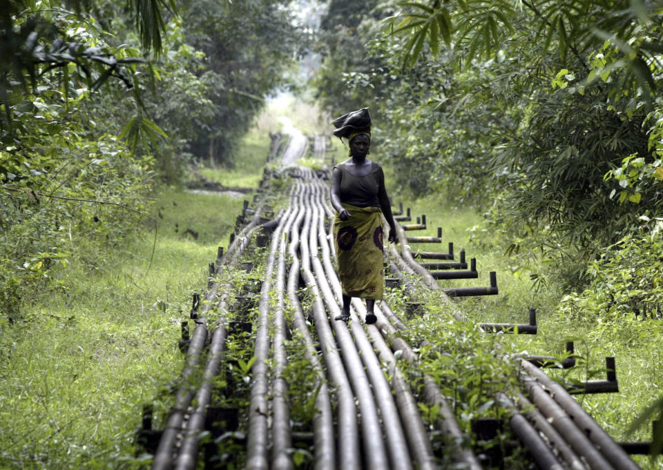 FILE- A woman walks along an oil pipeline in Warri, Nigeria, on Jan. 15, 2006. Nigerian state gas company has declared a force majeure after floods hindered gas operations, raising concerns among analysts about the West African nation's capacity to meet local and international demands. (AP Photo/George Osodi, File)