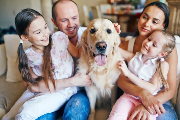 Man, woman, two girls, and a dog seated at a couch.