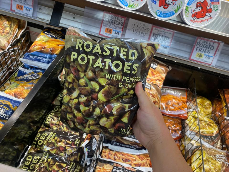 hand holding bag of roasted potatoes with pepper and onions in the freezer aisle at trader joes