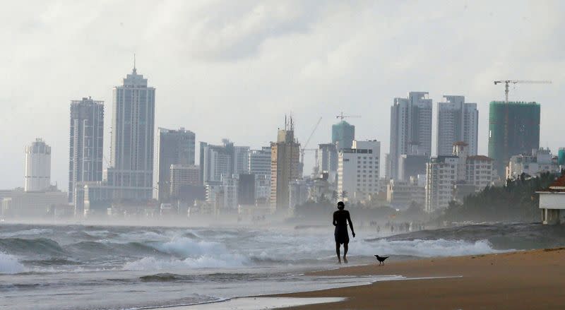 FILE PHOTO: A man walks along a beach, against the backdrop of Colombo's Financial City
