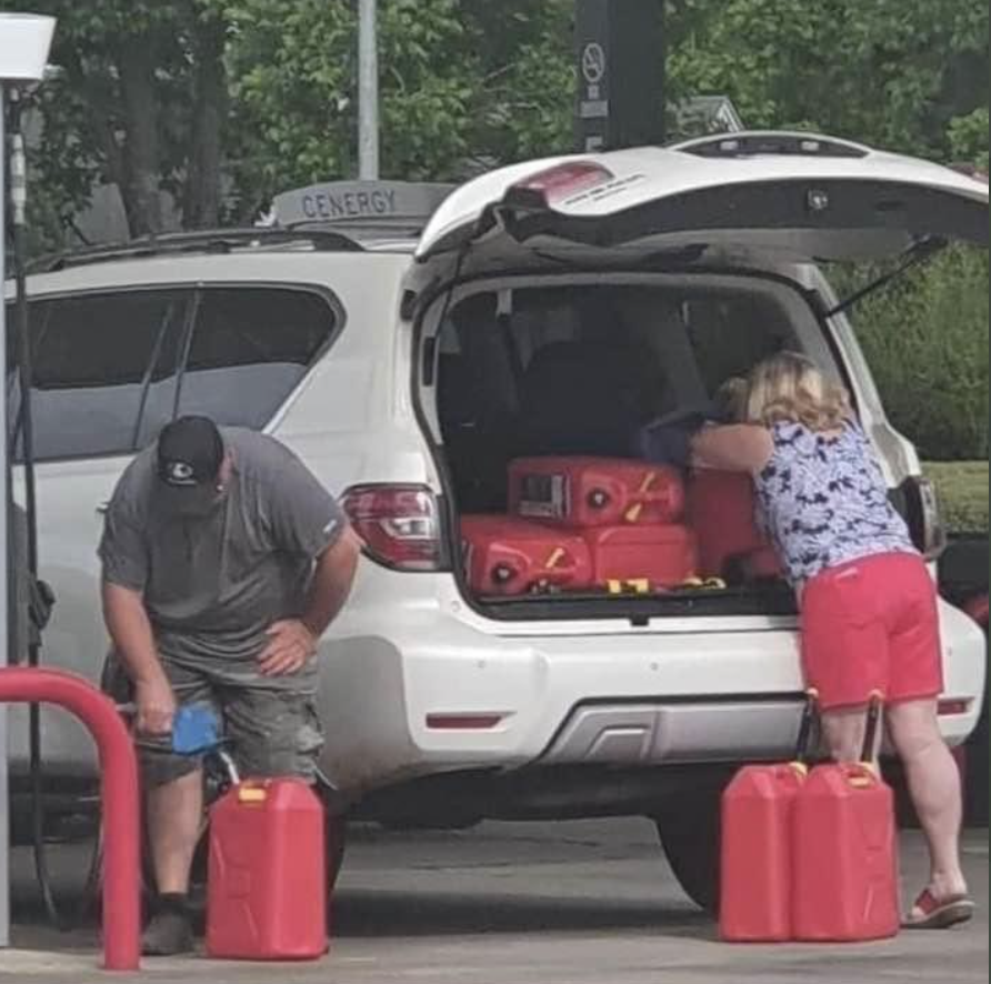 A couple appear to stockpile jerry cans of petrol, loading them into their car.