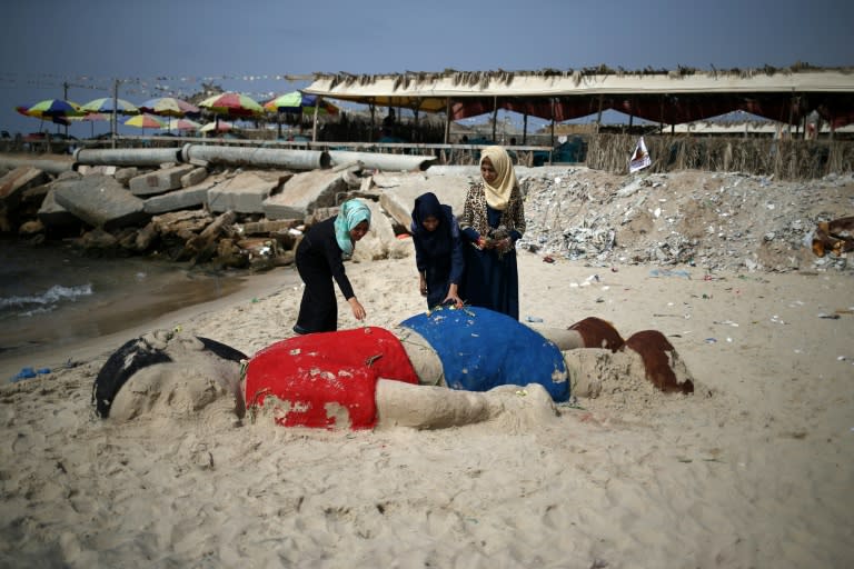 Palestinian girls put flowers on a sand sculpture depicting Syrian three-year-old boy Aylan Kurdi, who drowned off Turkey, on September 7, 2015, on Gaza city beach