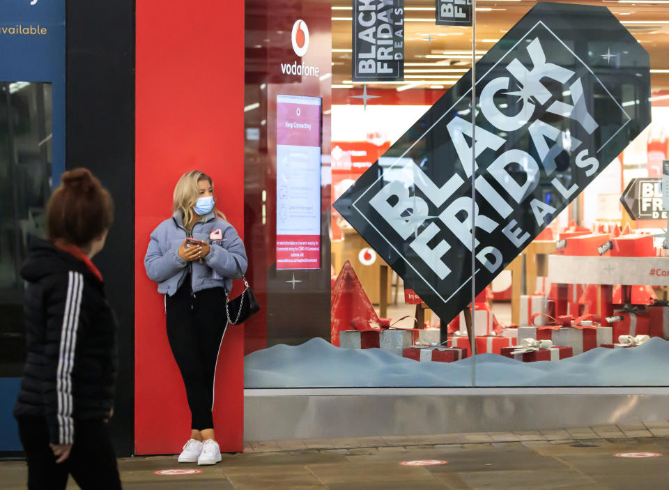 A woman next to a Black Friday poster in the window of a mobile phone store in Manchester city centre, England, although most stores remain closed Saturday Nov. 28, 2020. A four-week national lockdown to curb the spread of coronavirus is still restricting civil liberties and will put more pressure on shops to attract customers back to shopping streets when restrictions are relaxed in the run-up to Christmas. (Danny Lawson/PA via AP)