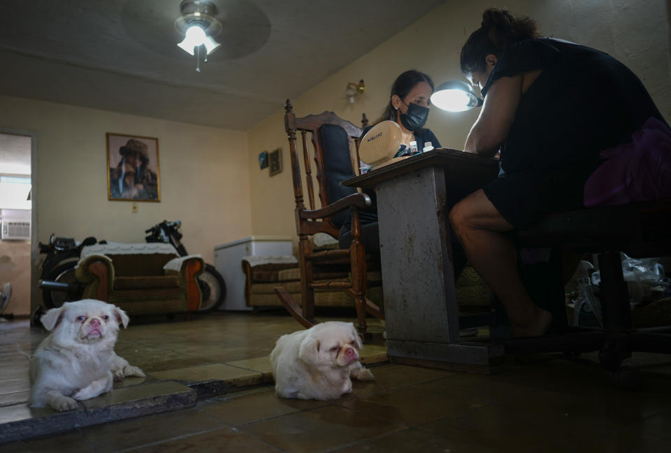 Marylin Alvarez, right, prepares a client's nails in the salon at her home as her two dogs lounge on the floor, at the Bahía neighborhood of Havana, Cuba, Wednesday, May 18, 2022. During President Barack Obama's administration, Alvarez began transforming part of her house into a tiny cafe with the help of money sent by a cousin living in the U.S., but it fell apart when President Donald Trump's administration tightened the embargo and sharply restricted money transfers to Cuba in late 2020, which turned Alvarez to a less costly form of making money for her family — giving manicures. (AP Photo/Ramon Espinosa)