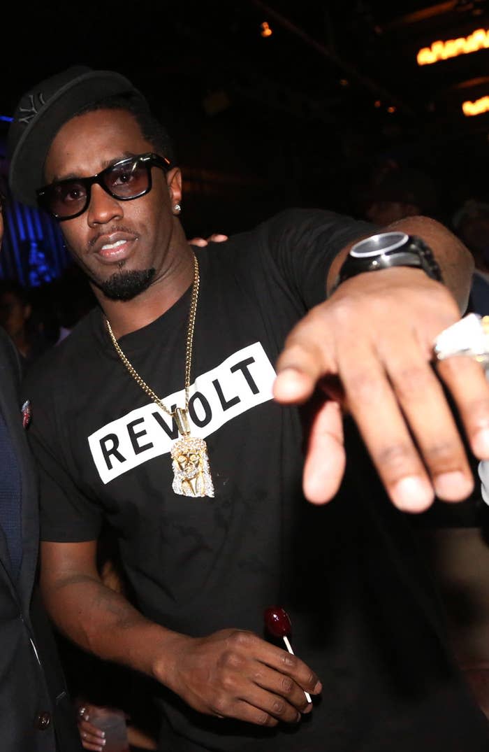 Sean Combs poses for a photo at a party while weearing a "Revolt" t-shirt and holding a sucker.