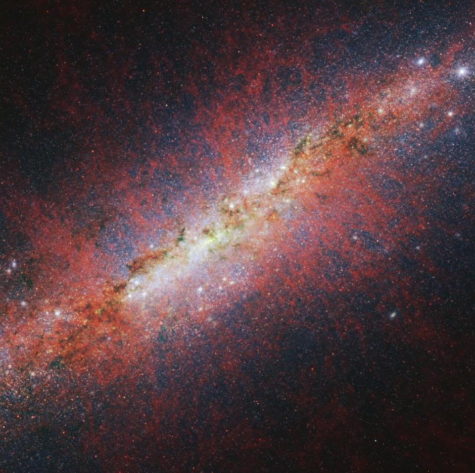 A reddish image of a galaxy seen from the side.  Lots of glitter everywhere.