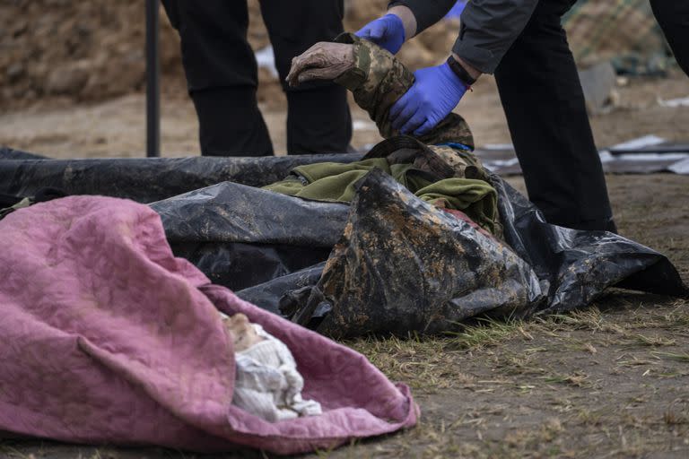 Un policía examina el cadáver de un soldado ucraniano sacado de una fosa común en Bucha, en las afueras de Kiev, Ucrania, el lunes 11 de abril de 2022