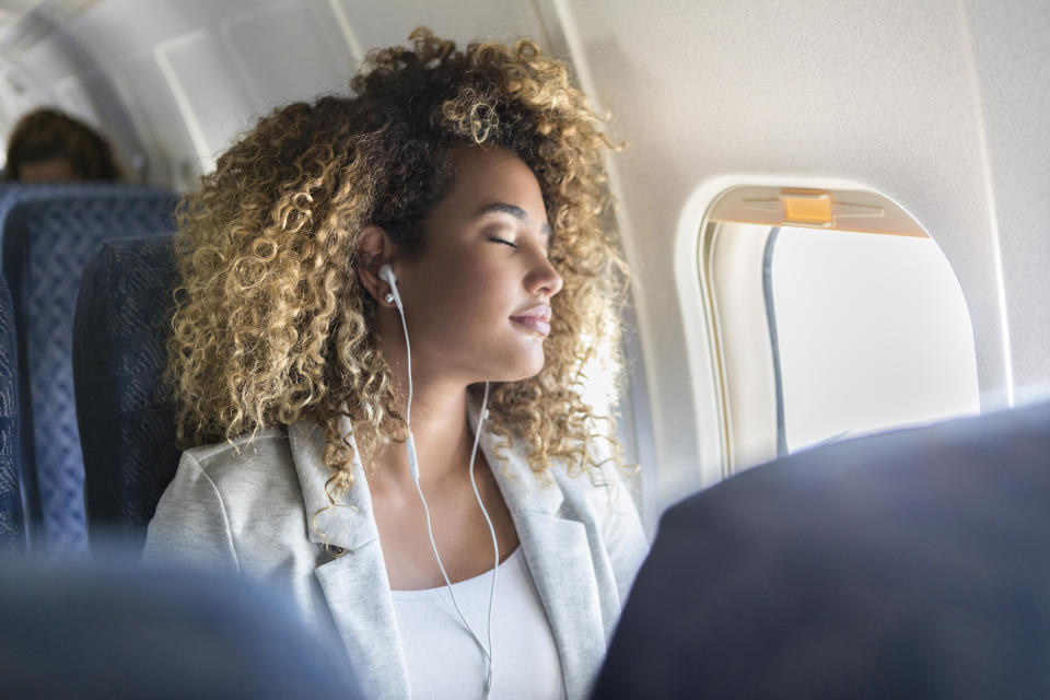 Attractive young woman naps during long airplane flight. She is wearing earbuds.