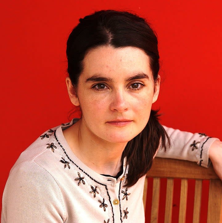 Shirley in embroidered top sitting, gazing at camera with a subtle smile