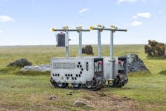 gray robotic machine on grassy low lying rocky heathland, blue sky