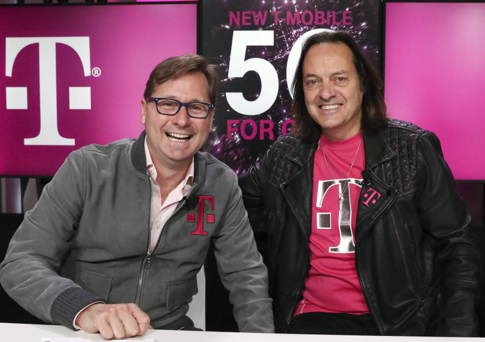 FILE - In this Nov. 7, 2019, file photo, T-Mobile President Mike Sievert, left, and CEO John Legere smile during a press conference in New York. T-Mobile says its colorful CEO John Legere is stepping down next year, even as the wireless company’s long-running effort to merge with rival Sprint remains unfinished. T-Mobile’s current president and chief operating officer, Mike Sievert, will become CEO in May after Legere’s contract ends. (Brian Ach/AP Images for T-Mobile, File)