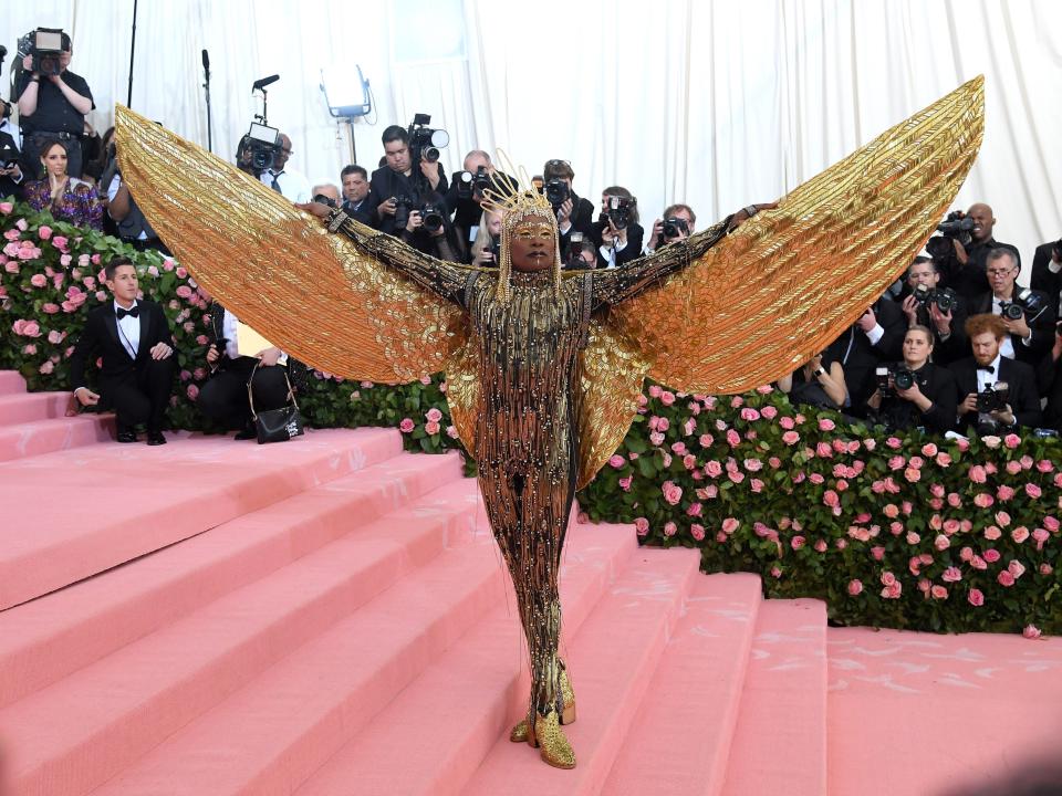Billy Porter at the 2019 Met Gala wearing a gold outfit with fringes and large gold wings