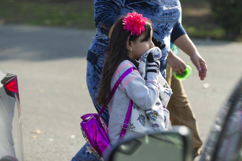 An unidentified girl covers her mouth as she evacuates the Park Avenue Elementary school in Cudahy, Calif., Tuesday, Jan. 14, 2020. Fire officials say fuel apparently dumped by the aircraft returning to LAX fell onto an elementary school playground. A fire department tweet says firefighters are assessing "multiple patients" at the school in the suburban city of Cudahy, Calif. (AP Photo/Damian Dovarganes)