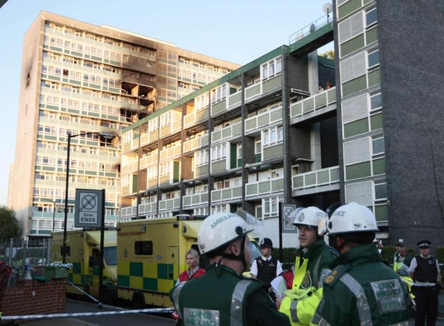 Firefighters and paramedics congregate outside Lakanal House in south London, with fire damage clearly visible on the upper floors.