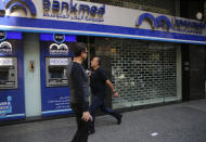 People pass by a closed bank, in Beirut, Lebanon, Wednesday, Oct. 30, 2019. Lebanese banks have been closed for the last two weeks as the government grapples with mass demonstrations that have paralyzed the country, but an even greater crisis may set in when they reopen Friday. (AP Photo/Hussein Malla)