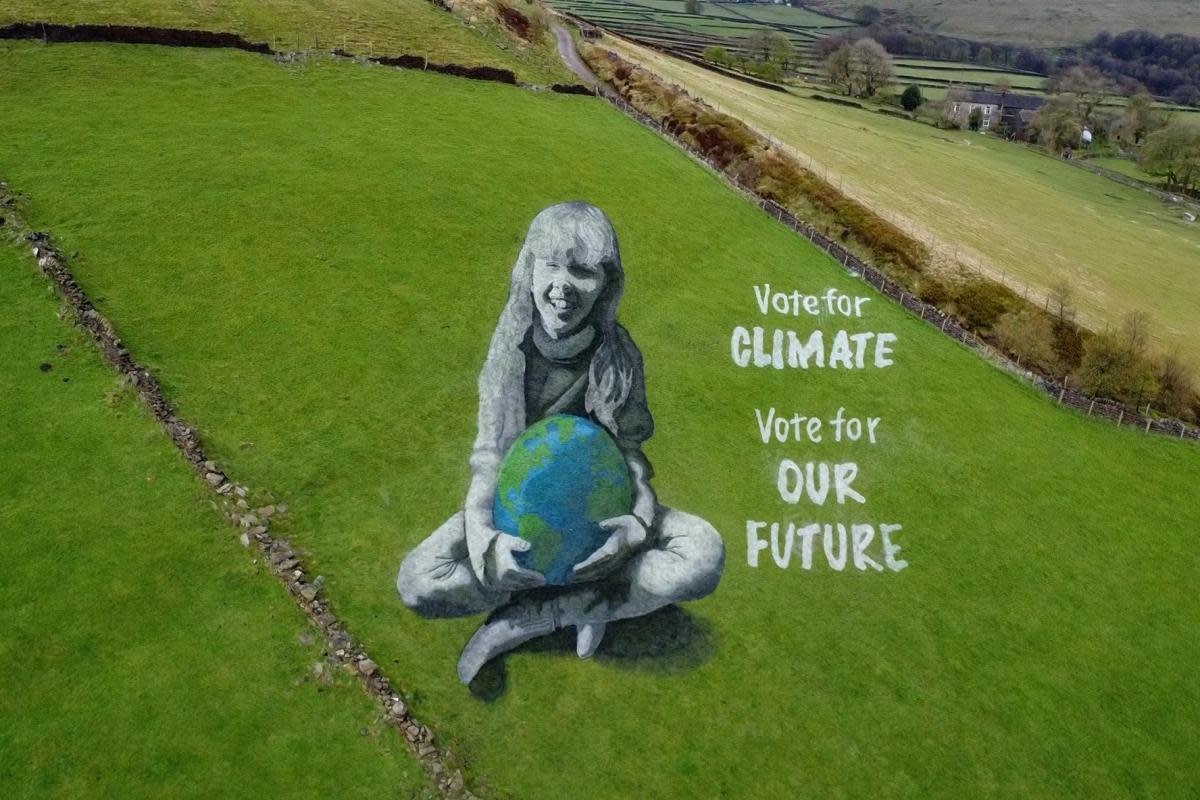 Bradford-born artist Jamie Wardley has created a 165ft (50m) high anamorphic painting of a girl holding the Earth in a Hebden Bridge field to mark Earth Day. <i>(Image: PA)</i>