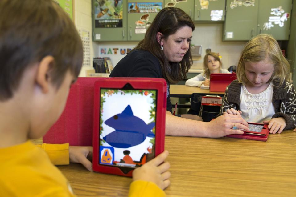 This photo taken Nov. 25, 2013 shows second grade teacher Heather Black working with Ingrid Soracco, 7, right, on her e-book assignment using an iPad at Jamestown Elementary School in Arlington, Va. Needed to keep a school building running these days: Water, electricity _ and broadband. Interactive digital learning on laptops and tablets is, in many cases, replacing traditional textbooks. Students are taking computer-based tests instead of fill-in-the bubble exams. Teachers are accessing far-off resources for lessons. (AP Photo/Jacquelyn Martin)