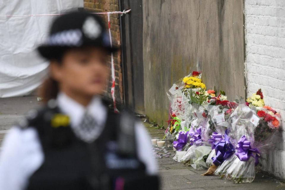 A police officer stands guard by floral tributes left at the scene of the fatal shooting in Tottenham (PA)