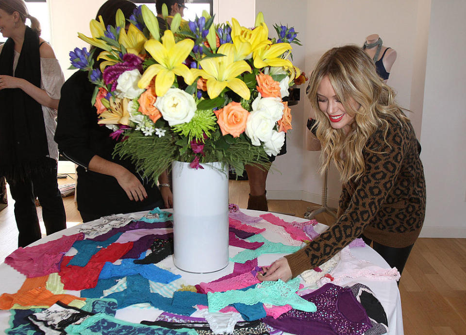 Hilary checking out a bunch of frilly underwear on a table with a vase of flowers