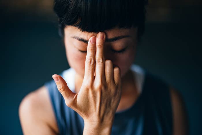 Person performing a yoga or meditation gesture with eyes closed, placing two fingers on their forehead