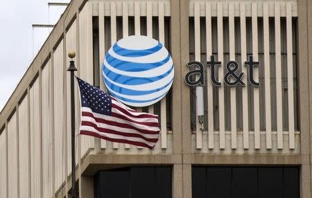 An AT&T Logo is pictured as a U.S. flag flutters in the foreground in Pasadena, California, January 26, 2015. REUTERS/Mario Anzuoni