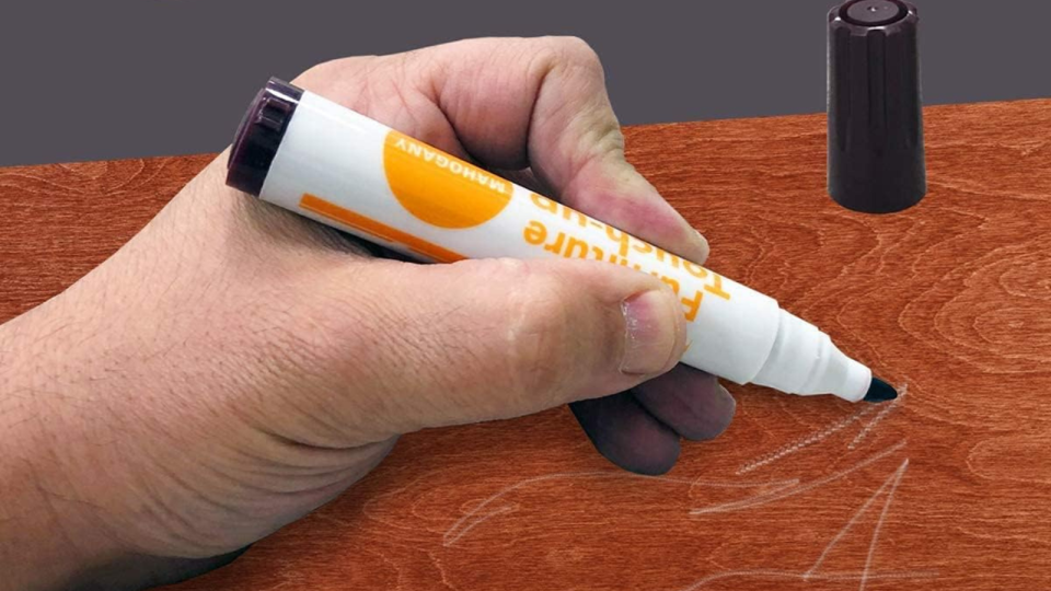 hand using a wood touch-up marker to cover scratches on a wooden furniture