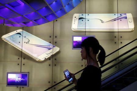 A woman holding an Apple iPhone passes a Samsung Galaxy S6 advertisement at a mall in Singapore in this April 24, 2015 file photo. REUTERS/Edgar Su/Files