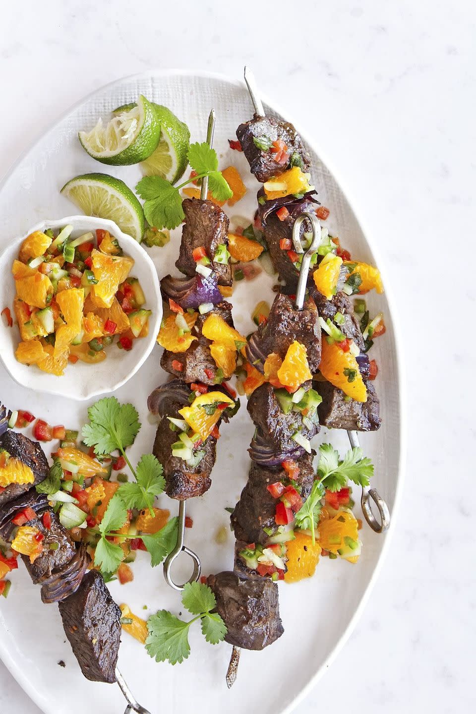 broiled steak kabobs on a white oval plate with a small bowl of orange relish