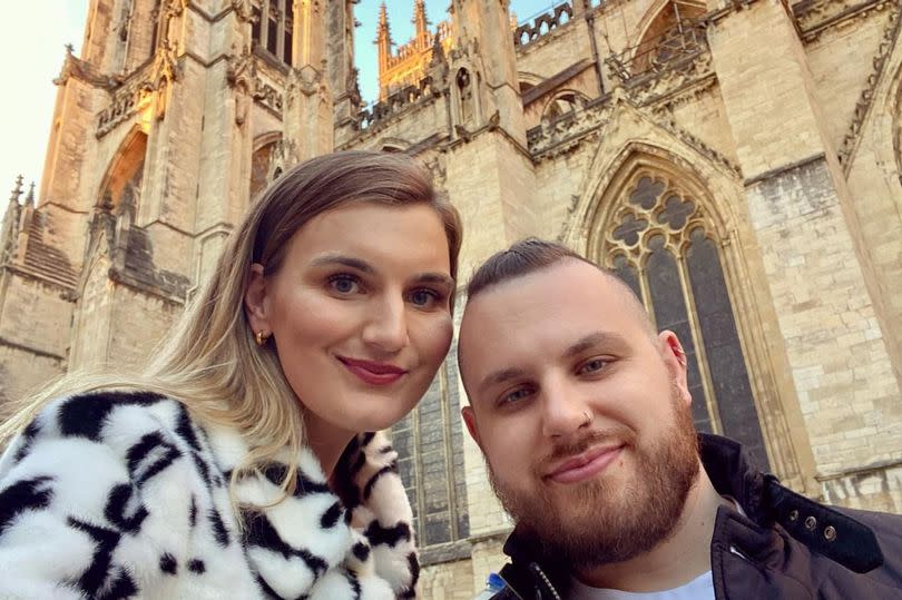 A woman posing for a selfie with her boyfriend outside a cathedral