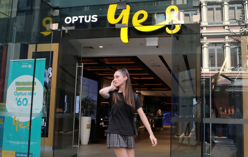 FILE PHOTO: A woman uses her mobile phone as she walks past in front of an Optus shop in Sydney